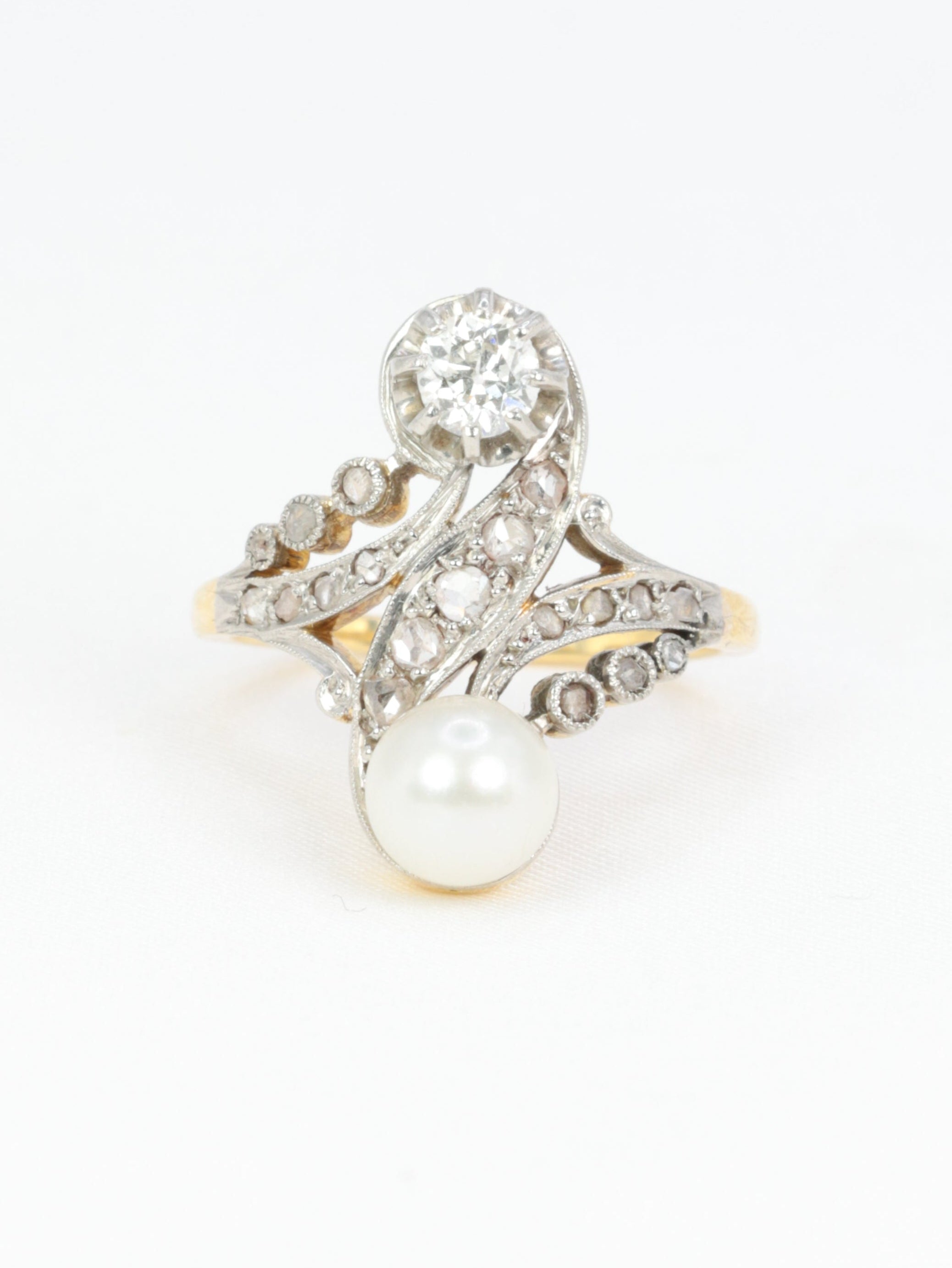 Bague toi et moi en or blanc 18k (750°/°°) et argent ornée d’une perle et d’un diamant old mine cut de très belle qualité pesant 0,4 carat soutenue par d’élégantes volutes pavées de diamants taillés en roses pour un poids total d’environ 1/2 carat. Longueur du motif : 2 cm&nbsp;Travail français des années 1910.&nbsp;Présence d’un poinçon tête d’aigle pour l’or 18 carats.

Poids brut : 5 grammes
